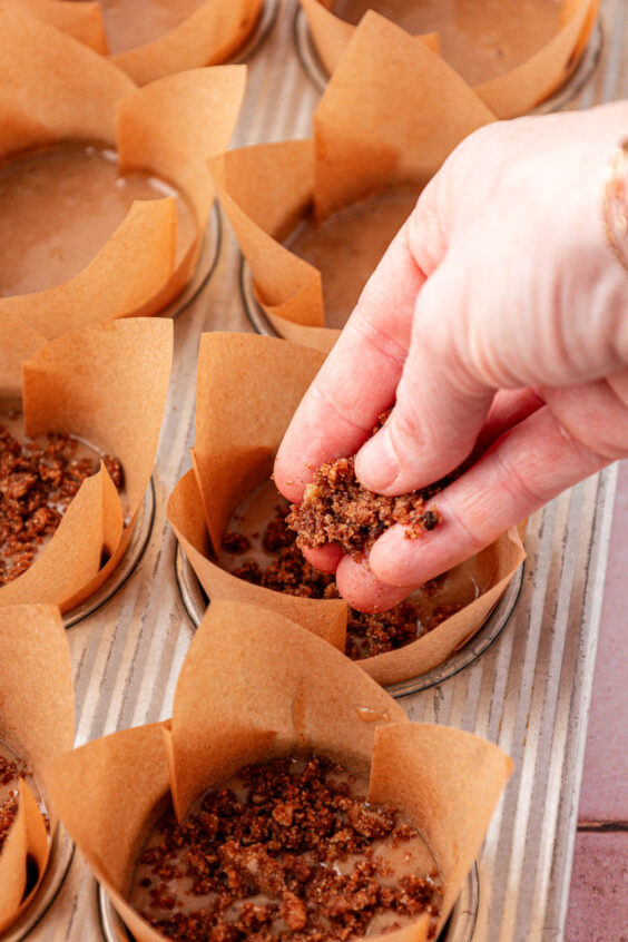Cinnamon crumble being sprinkled on the top of muffin batter.